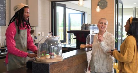 Barista with dreadlocks serving cupcakes to customers at bright modern coffeehouse