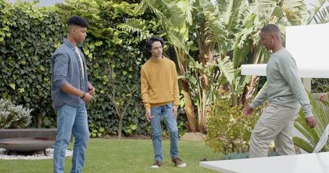 Three young men standing and talking on backyard lawn surrounded by tropical greenery