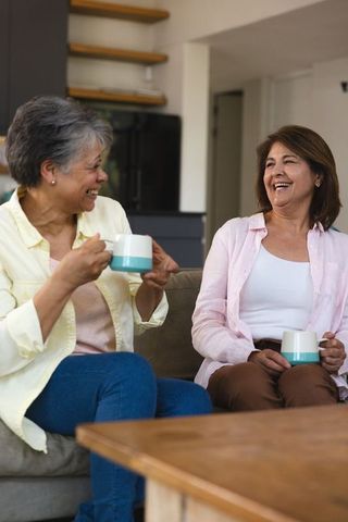 Diverse Female Friends Chatting and Relaxing on Sofa with Coffee Mugs
