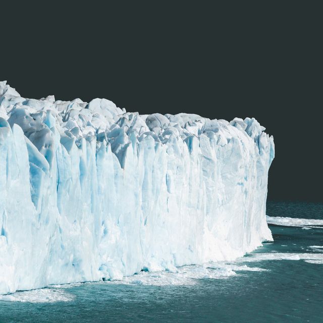This composition captures a massive iceberg glacier floating in Arctic waters. The sheer scale and detail of the ice formations are prominent against the dark backdrop. Ideal for use in environmental campaigns, climate change topics, travel blogs, nature documentaries, and educational materials about polar regions and ecosystems.