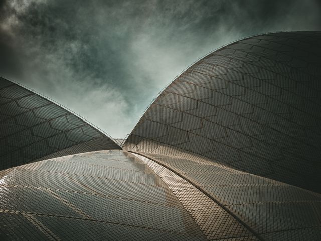 Stunning example of modern architecture, this photo features a crescent-shaped metallic dome building under a dramatic sky. Great for use in projects related to futuristic design, architecture, urban planning, and abstract art.