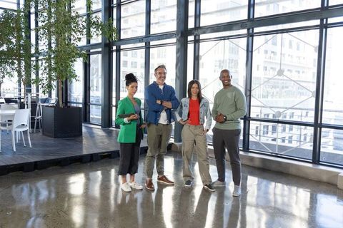 Diverse creative team standing in modern open-plan office with floor-to-ceiling windows