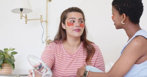 Friends sharing skincare rituals using under-eye gel patches in cozy bedroom