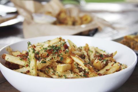 Garlic parmesan bacon fries in white bowl topped with parsley and crispy bacon crumbs