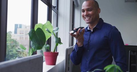 Smiling professional speaking into smartphone by office window