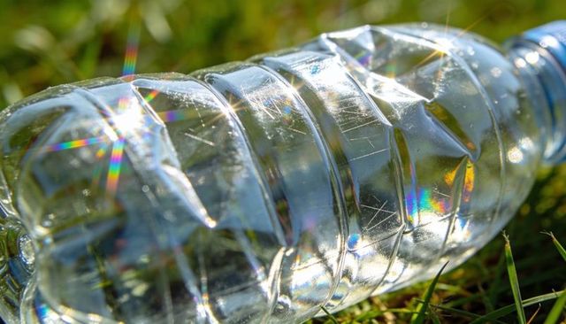 Crushed clear plastic water bottle on grass with iridescent sunlight and scratches