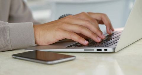 Typing male hands on silver laptop with smartphone nearby, minimalist modern workspace for productiv