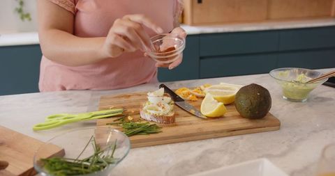 Sprinkling paprika over soft-boiled egg toast with avocado, lemon and fresh herbs