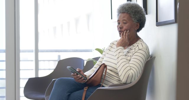 African american senior woman using smartphone in hospital waiting room. Medicine, healthcare, communication and medical services, unaltered.
