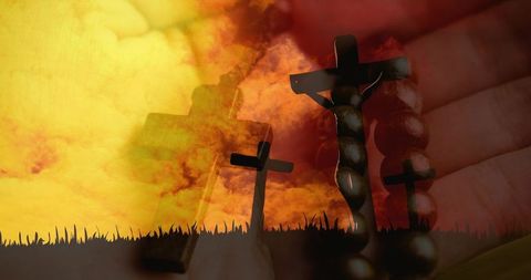 Holding rosary in palm with crucifix silhouetted against fiery sunset and three crosses