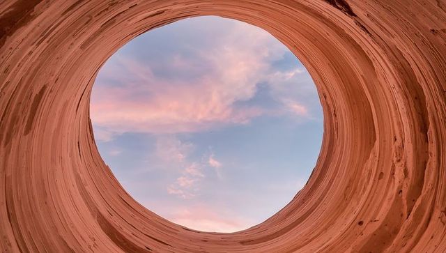 Circular canyon aperture framing pink sunset sky through eroded sandstone