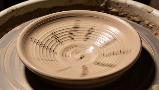 Spinning shallow clay plate on potter's wheel with radial tool marks and glossy glaze