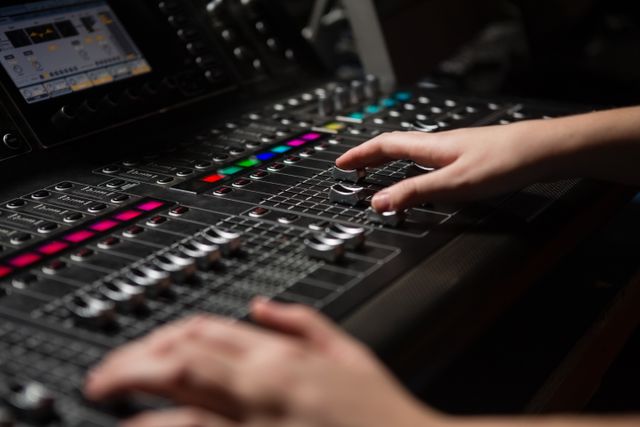 Hands of a female audio engineer operating a sound mixer in a recording studio, focusing on mixing and adjusting audio levels. This image is ideal for use in articles, blogs, and marketing materials related to music production, sound engineering, and professional recording. Perfect for illustrating technical skills in audio recording and production environments.