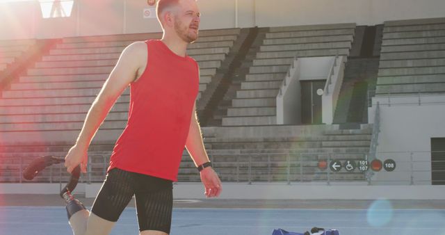 Man with a prosthetic leg walking on a track at a stadium in bright sunlight. The image can be used to represent athleticism, determination, and motivation. Suitable for advertisements, promotional materials, and articles on fitness, disability inclusion, and sports.