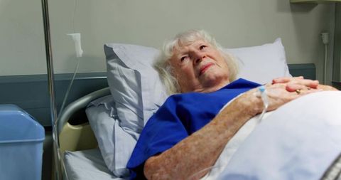 Senior woman resting in hospital bed with IV line looking hopeful during recovery
