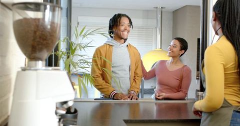 Smiling diverse couple chatting with barista at cozy modern espresso counter during morning