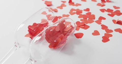 Champagne Flutes Spilling Red Heart Confetti on White Tabletop for Valentine