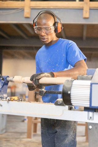 African american craftsman shaping wooden spindle on lathe wearing safety gear