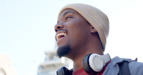 Laughing African American man looking up wearing beanie headphones and backpack in sunlight