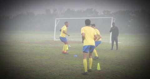 Youth soccer players practicing passing drill on foggy grass pitch with coach and cones