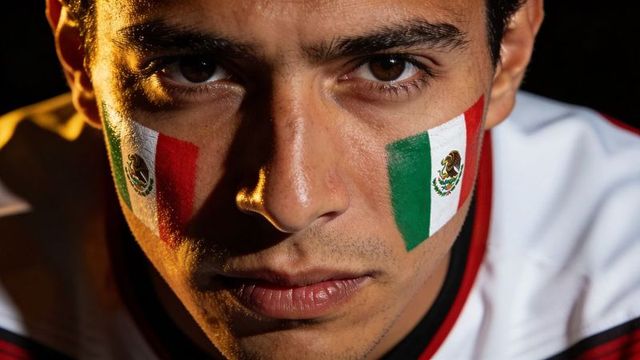 Intense mexican soccer fan wearing flag face paint and jersey closeup portrait dramatic light