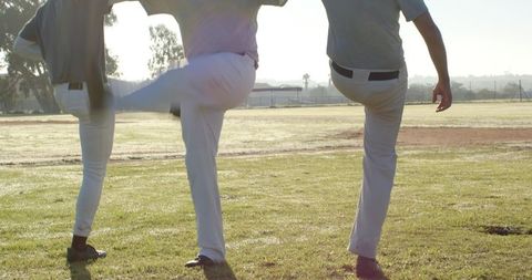 Male teammates performing synchronized high-leg kicks on grassy field during team warmup
