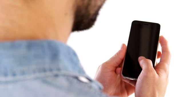 Close-up image showing a man using a smartphone. The man is wearing a denim shirt, and the focus is on his hands holding the phone. Ideal for advertising mobile apps, illustrating digital communication, or depicting modern technology usage.