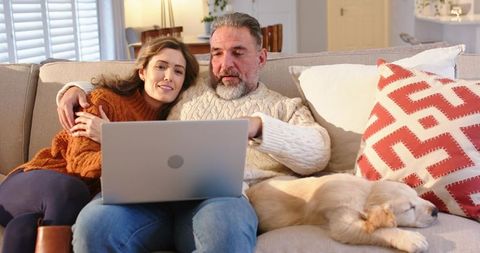 Mature Couple Relaxing on Sofa with Laptop and Sleeping Puppy, Cozy Home Evening