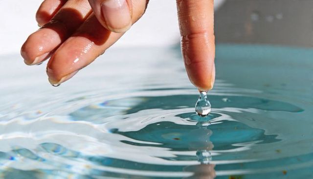 Fingertip Touching Water Droplet and Creating Circular Ripples on Blue Surface