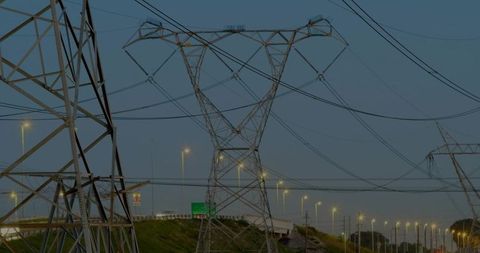 Electricity Transmission Towers at Dusk Illuminating Urban Highway