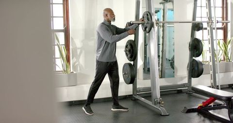 Mature African American Man Adjusting Barbell on Smith Machine in Bright Gym Strength Training