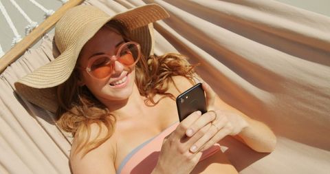 Woman Relaxing in Hammock Using Smartphone at Beach