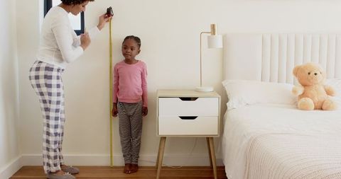 Mother Measuring Daughter's Height at Home in Bedroom