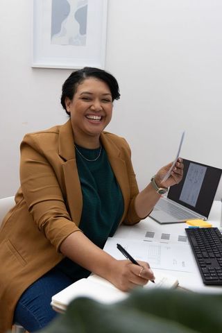 Smiling african american businesswoman writing notes at modern minimalist desk with laptop