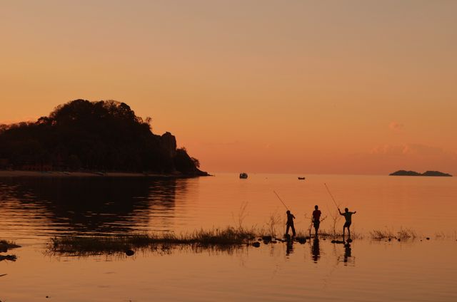Ideal for use in travel brochures, nature magazines, or websites promoting outdoor activities and serene getaways. This image captures the calm and beauty of the evening, making it perfect for advertising wellness retreats, vacation spots, or fishing gear. The silhouetted figures and warm tones add an element of tranquility and peacefulness.