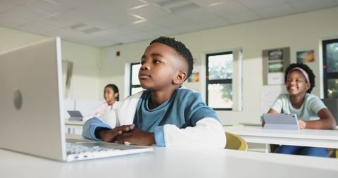 African American Boy Using Laptop in Modern Classroom with Diverse Classmates and Tablets