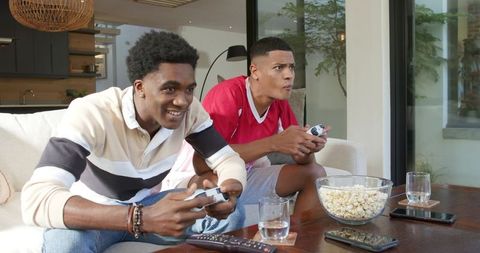 Excited Male Friends Gaming with Snacks in Modern Living Room