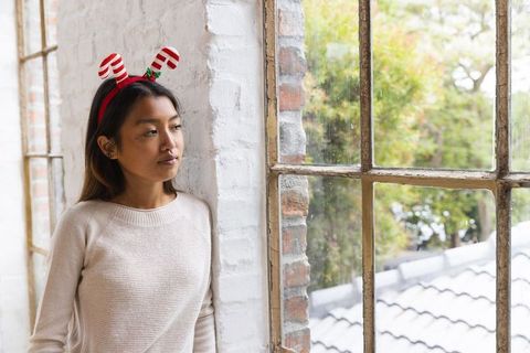 Reflective woman with festive antler headband near urban window