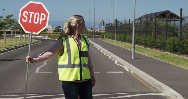 Caucasian lollipop woman with stop sign supervising sunny crossing outside elementary school. Summer, supervision, road safety, journey and school, unaltered.