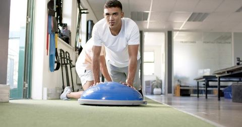 Athlete performing core stability push-up on blue bosu balance trainer on indoor turf