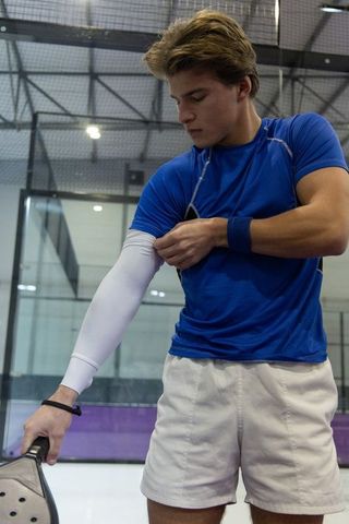 Padel player adjusting compression sleeve while holding racket on indoor glass court