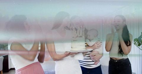 Women celebrating 30th birthday presenting cake and baby in cozy living room milestone