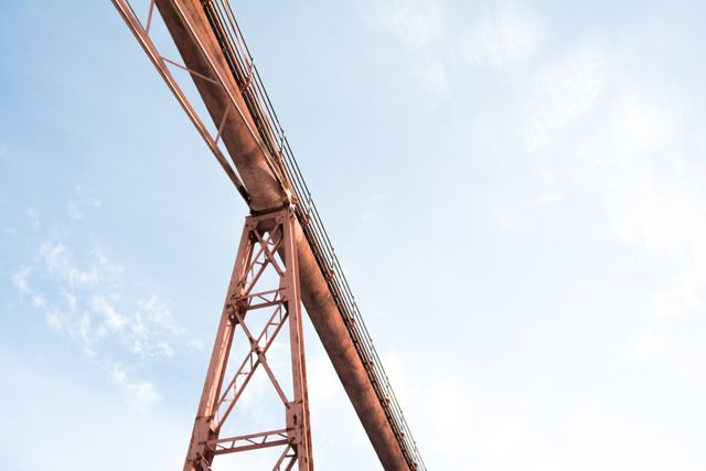 Depicting the underside of a red metal bridge against a clear blue sky, this image emphasizes strong architectural lines and industrial design. Suitable for use in articles on engineering, construction projects, architectural designs, urban development, and industrial photography. Perfect for business presentations, educational materials, or websites focused on infrastructure.