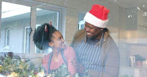 Diverse couple decorating kitchen with holiday garland, lights, aprons and santa hat