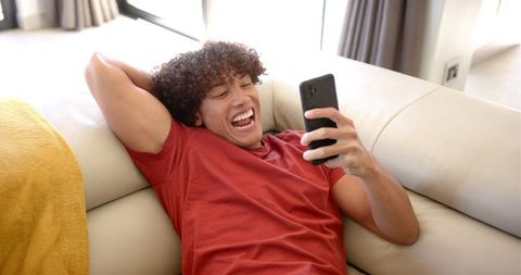 Happy young man relaxing on couch using smartphone at home
