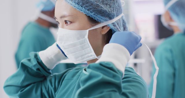 Image of asian female surgeon tying face mask in operating theatre, copy space. Hospital, medical and healthcare services.