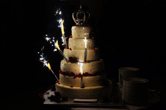 Opulent five-tier wedding cake adorned with sparklers in a dimly lit venue. Ideal for wedding-themed content, celebration invitations, event planning websites, and wedding blogs. Highlights elegance and festivity.