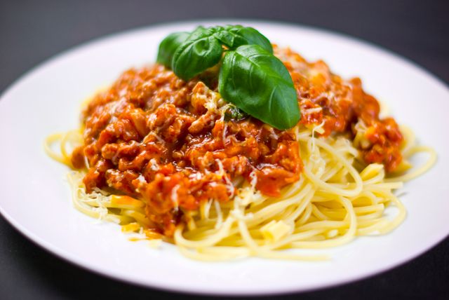 Appealing image of a plate of spaghetti Bolognese topped with a fresh basil garnish. Perfect for use in food blogs, recipe websites, cooking magazines, or restaurant menus. Highlights home-cooked Italian cuisine and can attract audiences looking for delicious and comforting meals.