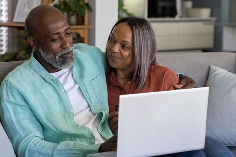 Senior couple using laptop on couch planning online banking and cozy home budgeting