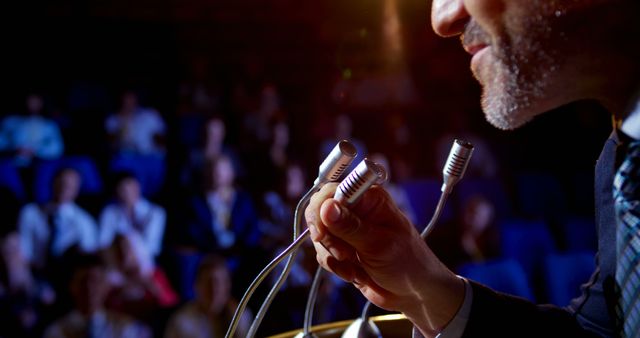 Mid section of mature Caucasian businessman speaking in business seminar on stage in auditorium. He is holding microphone 4k
